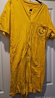 Full view of yellow romper on hanger, showing chest pocket graphic