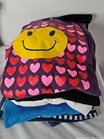 Stack of five folded vintage t-shirts, top is purple smiley heart tee