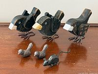 Group shot of three wood birds, two cast iron birds, one cast iron mouse on wooden surface