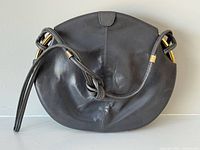 Front view of grey leather rounded purse showing gold-tone accents and knotted strap