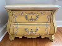 Front view of bombe nightstand showing finish, painted scrolls, hardware
