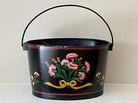 Front view of black metal bucket with floral painting and handle upright
