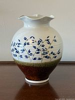 Front view of cream glazed vase with blue floral design, green and brown bands