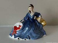 Front view of Royal Doulton Elyse figurine in blue dress holding white hat with red ribbon