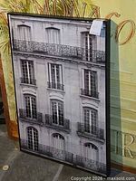 Framed black and white architectural print leaning against larger poster