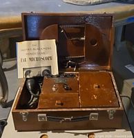 Closed wooden case opened showing microscope components, wiring, control panel and compartments