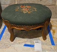 Top view of oval green needlepoint floral footstool showing upholstery and carved wood edge