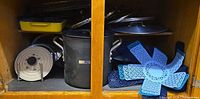 cabinet showing yellow enamel pan, stockpot, white lid, grill basket, lids, blue separators