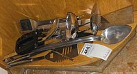 Pile of assorted stainless steel and plastic kitchen utensils on wooden shelf