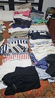 Overview of multiple stacks of folded women’s tops on bed