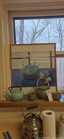 Group view of framed artwork, green teapot, cups, additional teapots