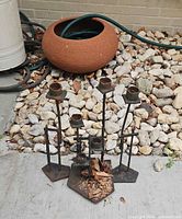 Clay garden hose pot, three iron candlesticks on concrete