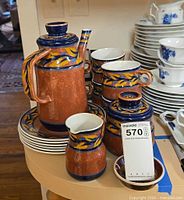 Group shot of full pottery set on counter showing lidded pot, stack of cups, creamer, sugar bowl, trinket dish