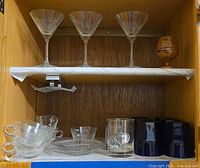 Cabinet shelf with martini glasses, plates, teacups, tumblers, wooden egg