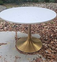 Full view of white round tabletop on gold pedestal base outdoors