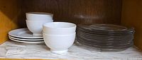 Stack of white bowls and plates beside stack of clear plates
