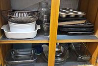 Cabinet view showing ceramic casserole, fluted bowl, glass jars, muffin pan, springform pans, metal bakeware, glass bakeware