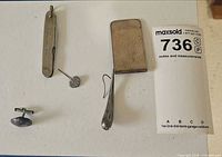 Group shot showing all five items: money clip, pocket cutter, pin, cufflink, earring