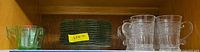 Green depression glass creamer, stack of ivy-trimmed plates, four crystal mugs on shelf