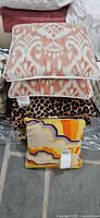 Stack of three pillows: coral/white ikat, leopard print, multicolour tapestry