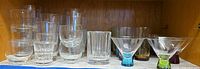 Shelf view showing stacked clear lowballs, rounded tumblers, faceted rocks glass, martini glasses and colored-base highballs