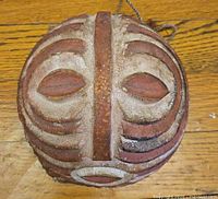 Front view of oval carved wooden mask showing stylized facial features and paint remnants