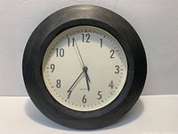 Front view of black wood wall clock showing face and frame