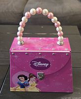 Front view of pink Disney Princess tin purse showing Snow White and Belle graphics, beaded handle and latch