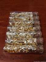 Seven cork-stoppered glass vials filled with gold leaf flakes aligned on wooden surface