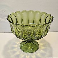 Front view of olive green pressed glass pedestal compote bowl showing scalloped rim and footed base