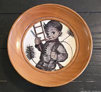 Front view of wooden musical plate showing illustrated ceramic center