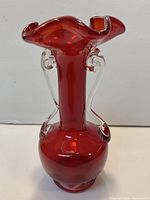 Front view of ruby red art glass vase showing ruffled rim and clear applied handles