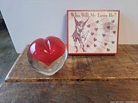 Glass heart paperweight beside romance predictor game box top