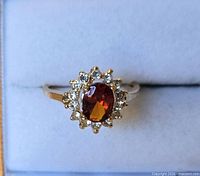 Top view of ring showing oval red/orange stone and surrounding clear stone halo
