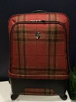 Front view showing plaid fabric, logo badge, zip pocket, plastic base and wheels