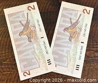 Front and back of both consecutive 1986 $2 Canadian banknotes on wooden surface