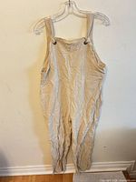 Front view of beige strap overalls hung on hanger
