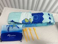 Folded blue patterned beach mat, Diveblues pouch, four yellow stakes on table