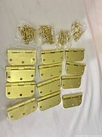Twelve brass butt hinges laid out with six bags of matching screws