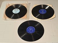 Three black vinyl LP records with blue labels, two on partial inner sleeves, jackets absent