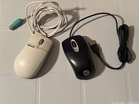 Top view of two wired mice showing Logitech black optical mouse and Microsoft white ball mouse with cords