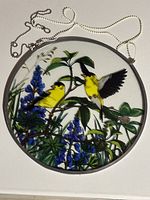 Front view of round stained-glass sun catcher showing goldfinches, flowers, metal frame, and hanging chains