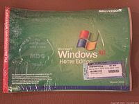 Front view of sealed Windows XP Home Edition OEM CD sleeve showing branding, version, shrink wrap, and COA label