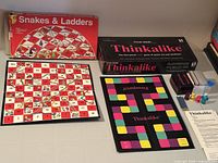 Both game boxes, Thinkalike contents laid out, Snakes & Ladders board visible
