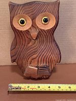 front view of carved wooden owl with measuring tape showing height ~8 in