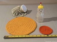 All items laid out with tape for scale: ice pack, Billy Bee bottle, yellow and orange doilies