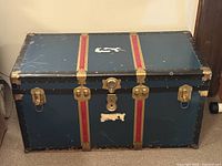 Closed blue metal steamer trunk showing exterior condition, brass hardware and red stripes