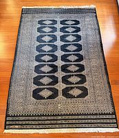 Full view of black and tan Turkish rug showing pattern and fringe