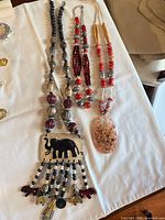 All three necklaces laid out: elephant pendant, red bead, coral-tan pendant