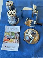 All components laid out on blue background: two cones, base with crank, chute, domed part, booklet